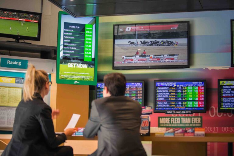 Patrons watching live data feed graphics on digital display. Live graphics and real data display in DIGITAL DISPLAYS / TICKERS | Automated graphics. Content management and automated graphics solutions. Content examples include live scores, upcoming events, live odds, venue promotions etc. Catering to all LED screen types (ribbon screens, digital signage, scoreboards, video walls). Digital information display solutions